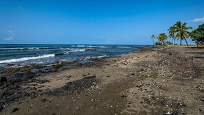 Una playa con arena oscura, rocas dispersas y olas.