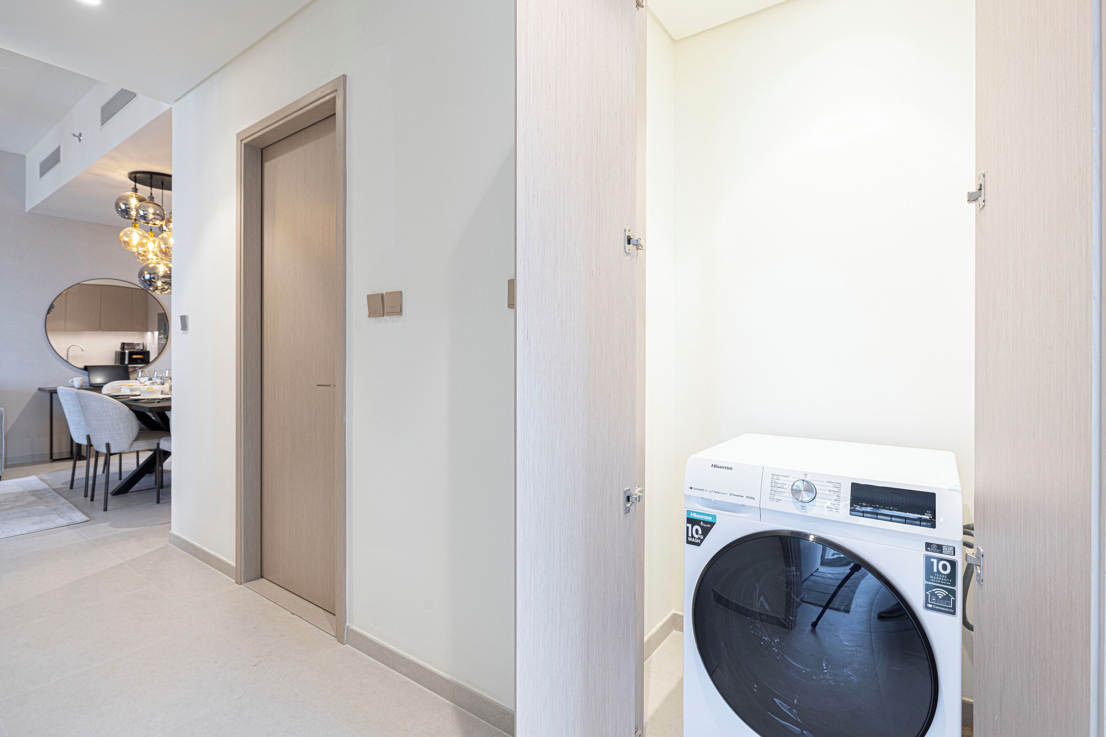 A laundry room with a front-loading washing machine, a wooden door, and a dining area with a table and chairs.