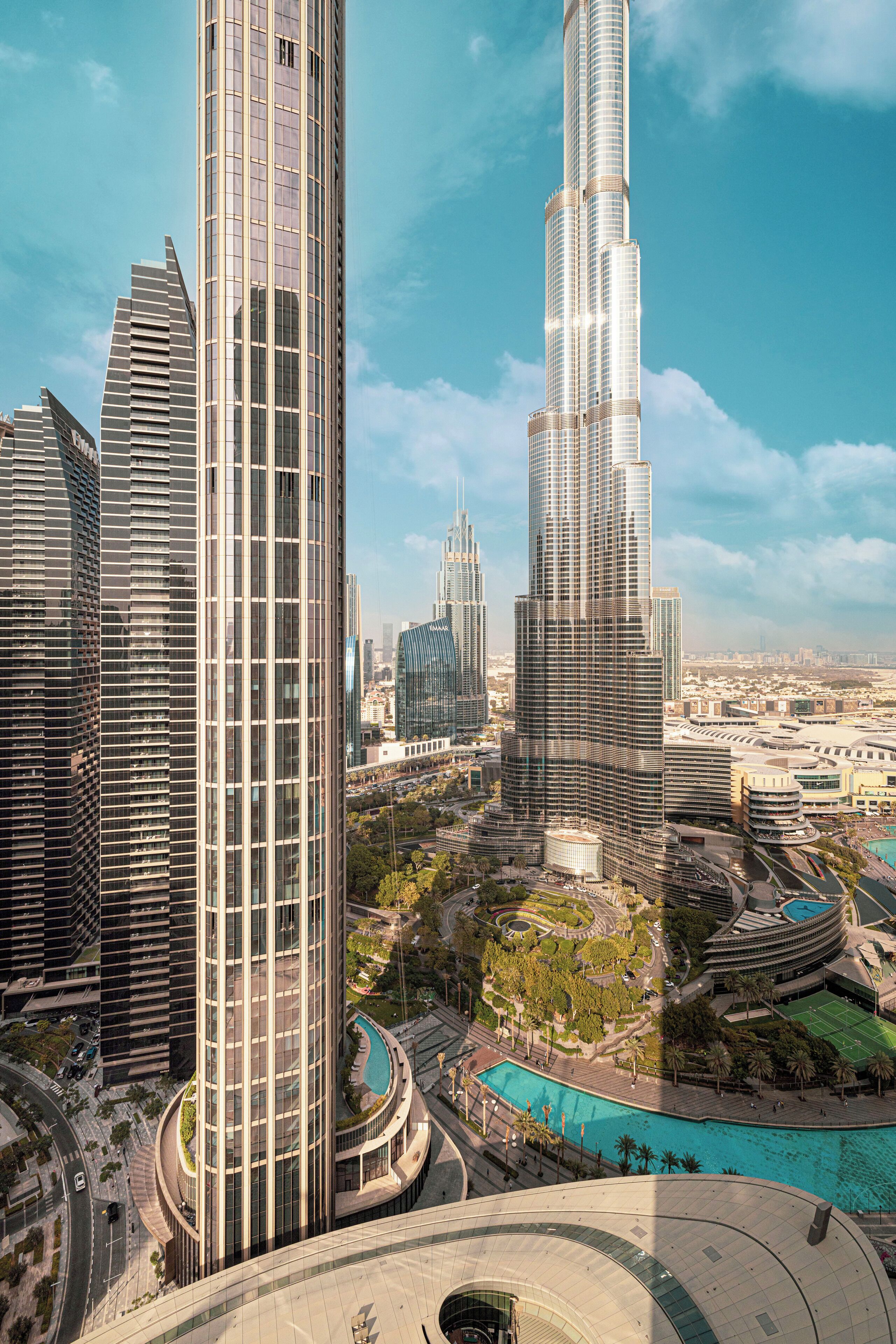 Un immeuble de grande hauteur à la façade incurvée, entouré d’autres gratte-ciel modernes et d’un espace paysager agrémenté d’une piscine.