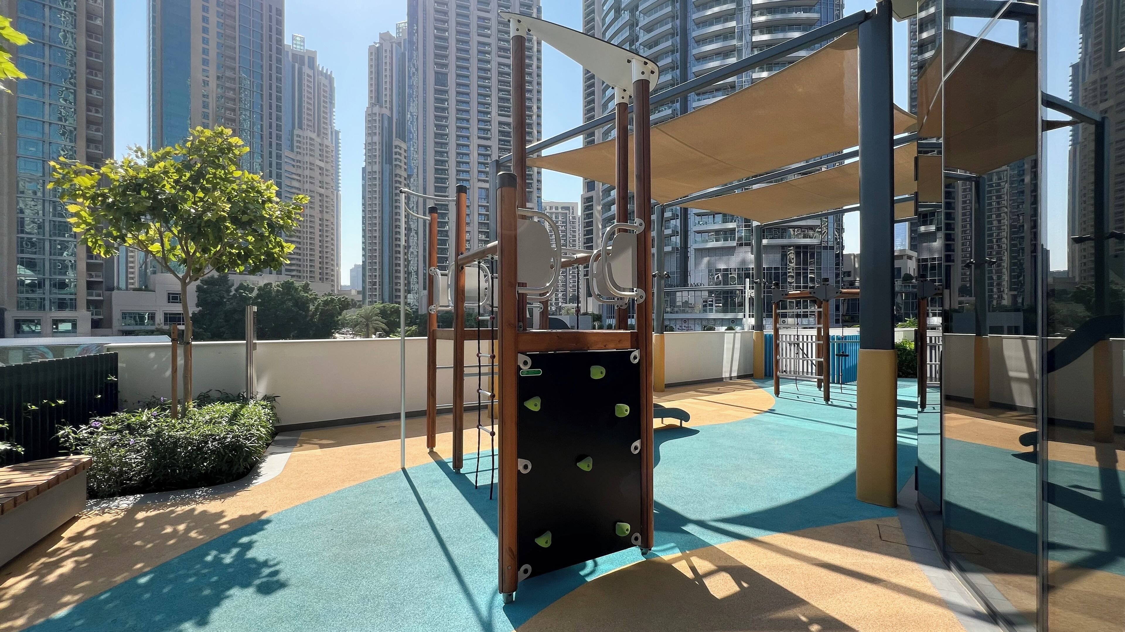 Ein Spielplatz im Freien mit Klettergerüsten und einem blau-beigen Spielbereich, umgeben von hohen Wohnhäusern.