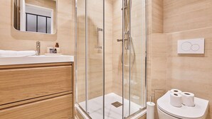 A modern bathroom with a glass-enclosed shower, wooden cabinetry, a white sink, and a toilet with toilet paper. - THE Parisian SUITE / Center of Paris (Paris)