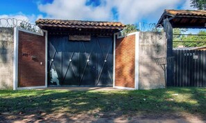 A gated entrance with a metal gate, a brick wall, and a sign above the gate. - Casa de campo em Cotia com piscina e lazer (Cotia)