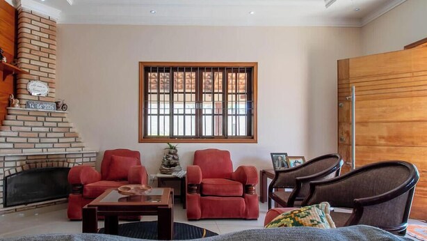 Una sala de estar acogedora con chimenea de ladrillo, sillones rojos, una mesa de centro de madera y un televisor montado en la pared.
