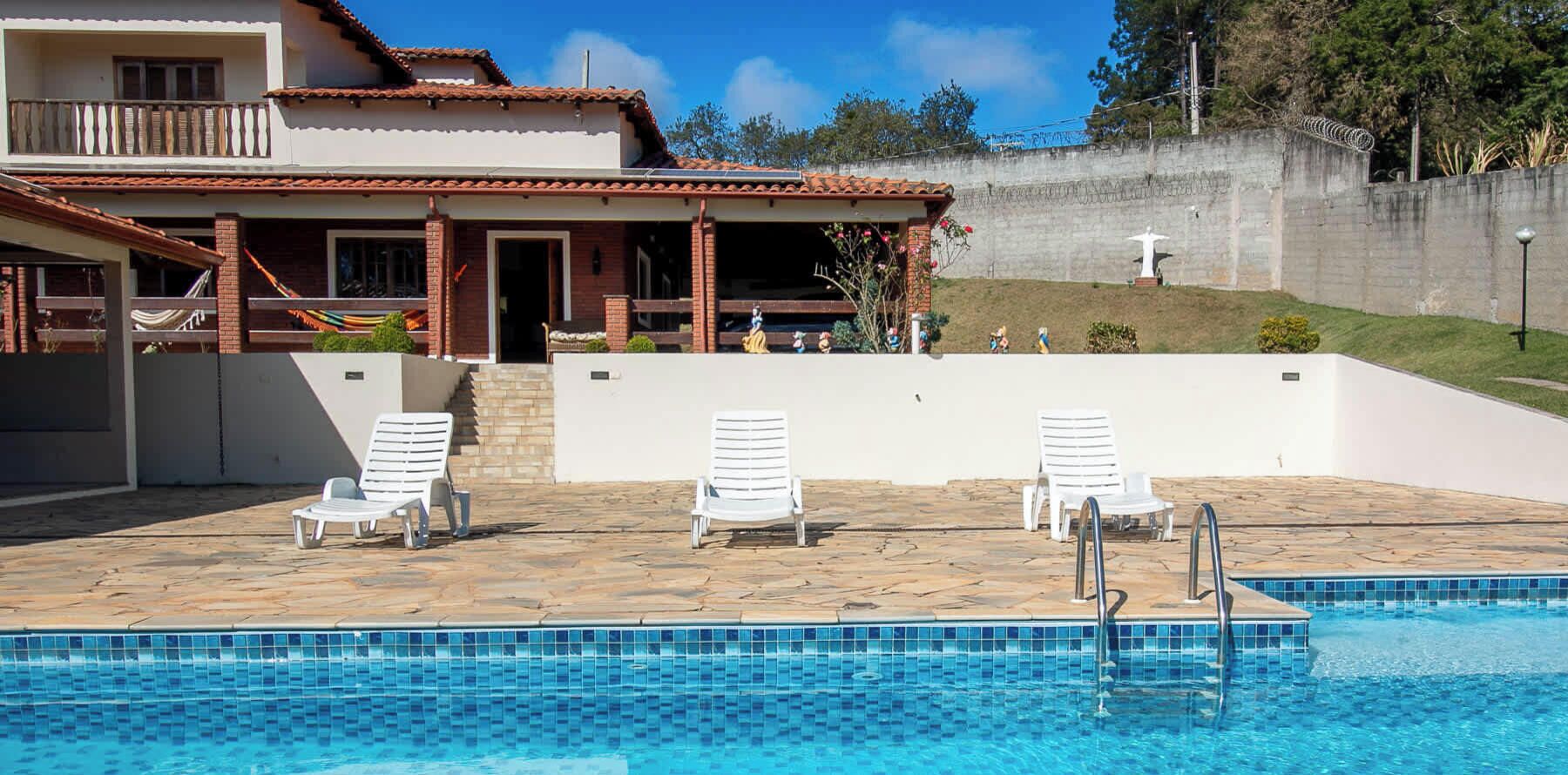 Una piscina amb gandules blanques, un solàrium amb rajoles i una casa amb un balcó al fons.