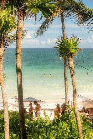 Een strand met palmbomen, helder turquoise water en mensen die zwemmen en ontspannen op het zand.