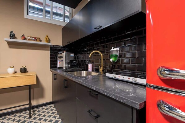 Una cocina moderna con un salpicadero negro, un lavamanos de acero inoxidable y un refrigerador rojo.