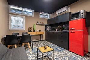 Una cocina compacta con un refrigerador rojo, una mesa de comedor con sillas y una pequeña mesa auxiliar.