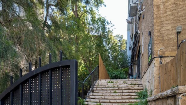 Eine Treppe aus Stein führt zu einem verschlossenen Eingang, umgeben von Bäumen und einem Gebäude mit einer Steinfassade.