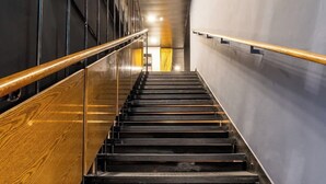 Eine Treppe mit Metallstufen und Holzhandläufen, die zu einem Raum mit einem gelben Vorhang führt.