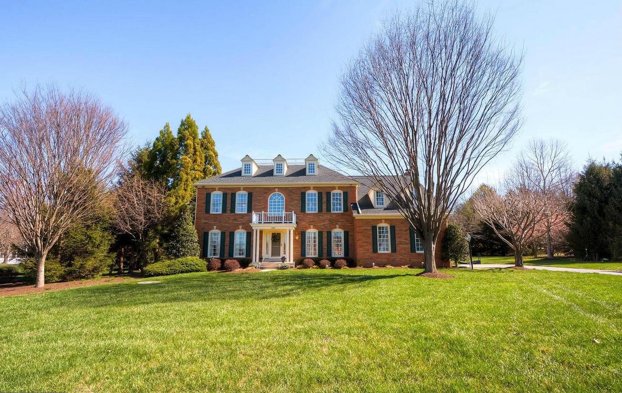A large brick house with a front porch, surrounded by a well-maintained lawn and trees.