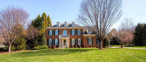 A large brick house with a front porch, surrounded by a well-maintained lawn and trees.