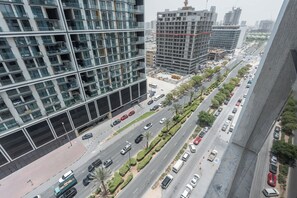 A multi-story building with a modern glass facade, a busy urban street with cars, and construction sites in the background. - StayShort - Comfy JVC Retreat for 2 with Pool & Gym (JVC)