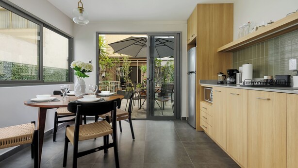 Una cucina moderna con mobili in legno, un'area pranzo con tavolo apparecchiato per quattro e vista su un patio esterno con ombrelloni.