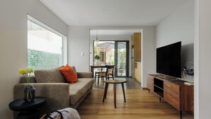 Un soggiorno moderno con divano, tavolino da caffè e mobile TV. Si intravede, attraverso una porta aperta, un'area pranzo con sedie e tavolo.