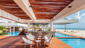 A poolside area with a wooden deck, white lounge chairs, and a bar area overlooking the beach. - La Amada Private Terrace (Cancún)