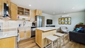 Une cuisine moderne avec des meubles en bois, un réfrigérateur encastré et un îlot central. On y trouve également un coin repas avec un canapé et un téléviseur.