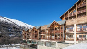 A multi-story wooden lodge with balconies and large windows, set against a snowy mountain backdrop. - Le Hameau de Valloire S4p Coin Nuit (Valloire)
