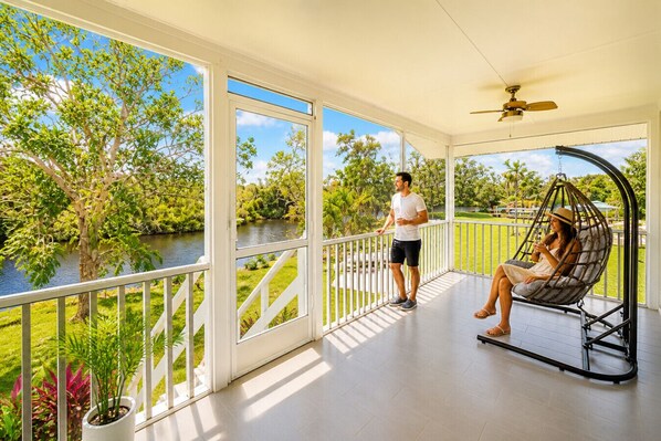 A covered outdoor area with a view of a river, a swing chair, and a person standing.