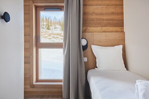 Une chambre à coucher avec une tête de lit en bois, une fenêtre donnant sur des arbres et un lit avec une literie blanche.