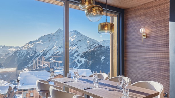 Un comedor con una mesa dispuesta para cuatro, ventanas amplias que ofrecen vistas a la montaña, e iluminación colgante.