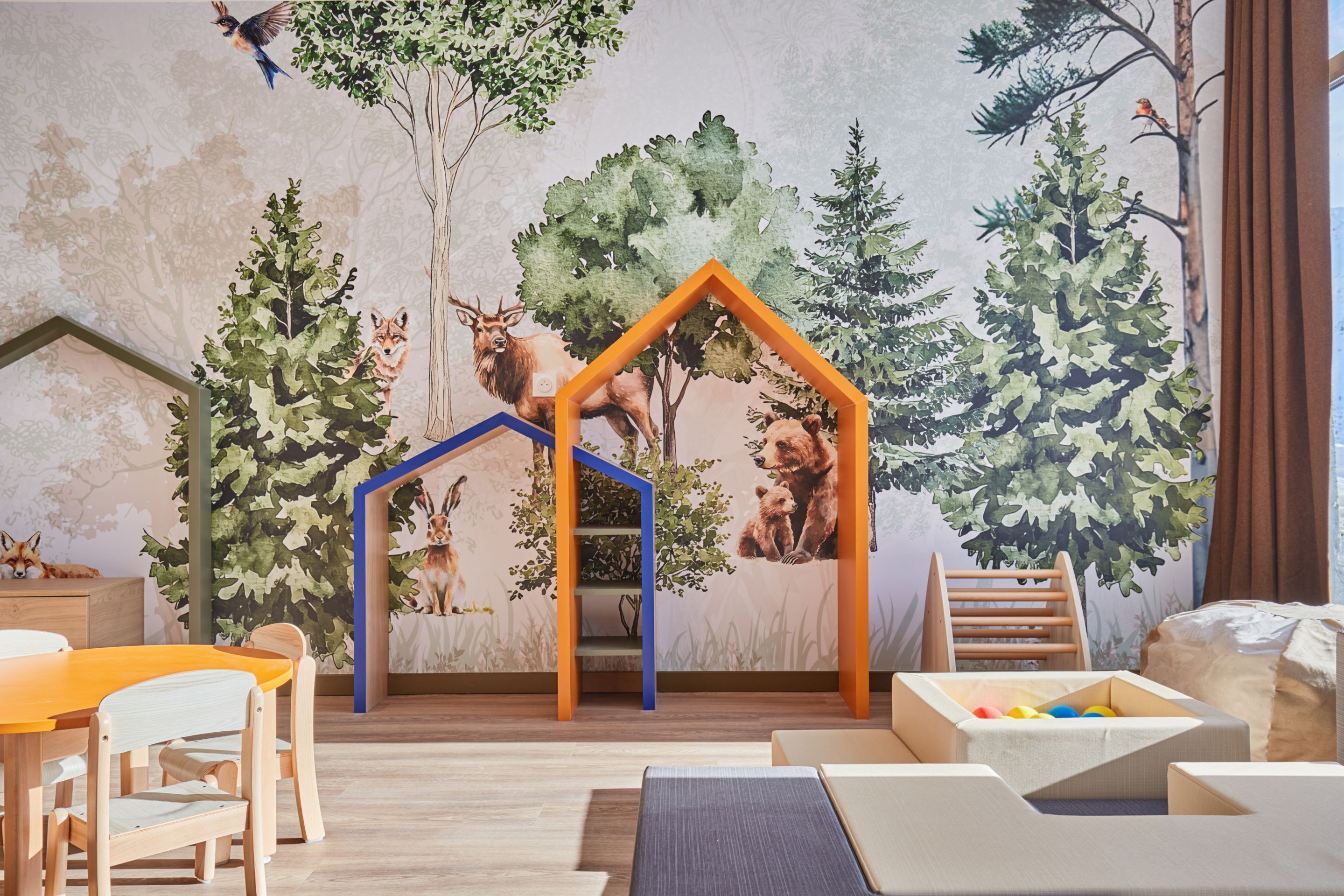 Un cuarto de juegos infantil con un mural, una casita de madera y una mesa con sillas.