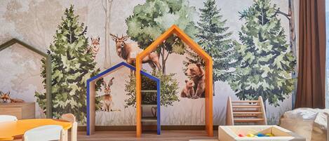 Un cuarto de juegos infantil con un mural, una casita de madera y una mesa con sillas.