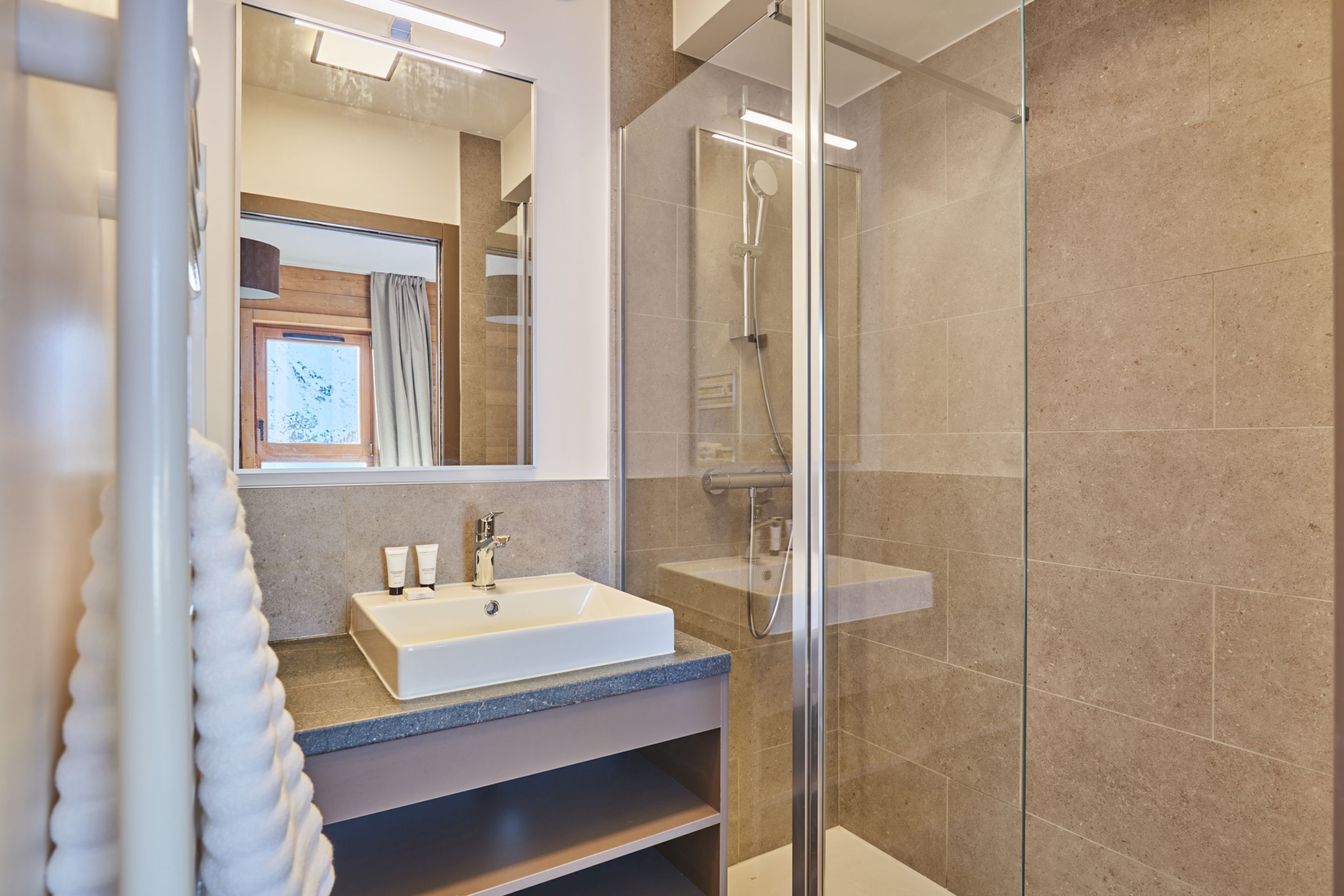 Ein modernes Badezimmer mit einer Duschkabine aus Glas, einem weißen Waschbecken mit Marmorplatte und einem großen Spiegel.