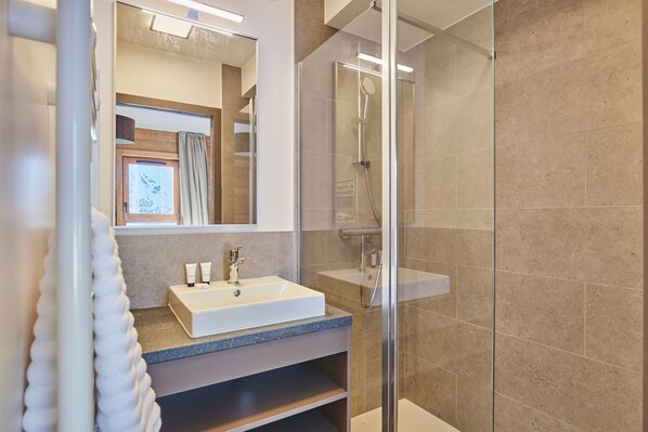 A modern bathroom with a glass shower enclosure, a white sink with a marble countertop, and a large mirror.