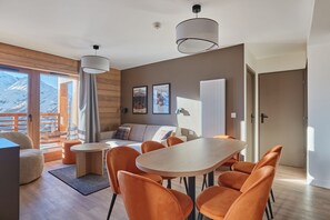 Et moderne interiør med trægulv, et rundt bord med stole, en sofa og udsigt til bjerge.