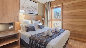 A wooden-paneled room with a bed, a bedside table, a wall-mounted light, and a window with a view of mountains.