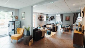 A spacious living area with a sofa, armchair, and coffee table, a dining area with chairs and a table, and a kitchen in the background.