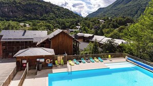 A pool area with lounge chairs, a wooden building, and a mountainous backdrop.