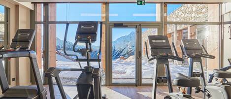 A gym with treadmills, ellipticals, and a large window with a mountain view.