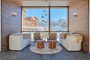 A modern interior with a large window, two sofas, two wooden tables, and wall-mounted light fixtures. - Suite Familiale | À 100m des Pistes | Piscine (Montvalezan)