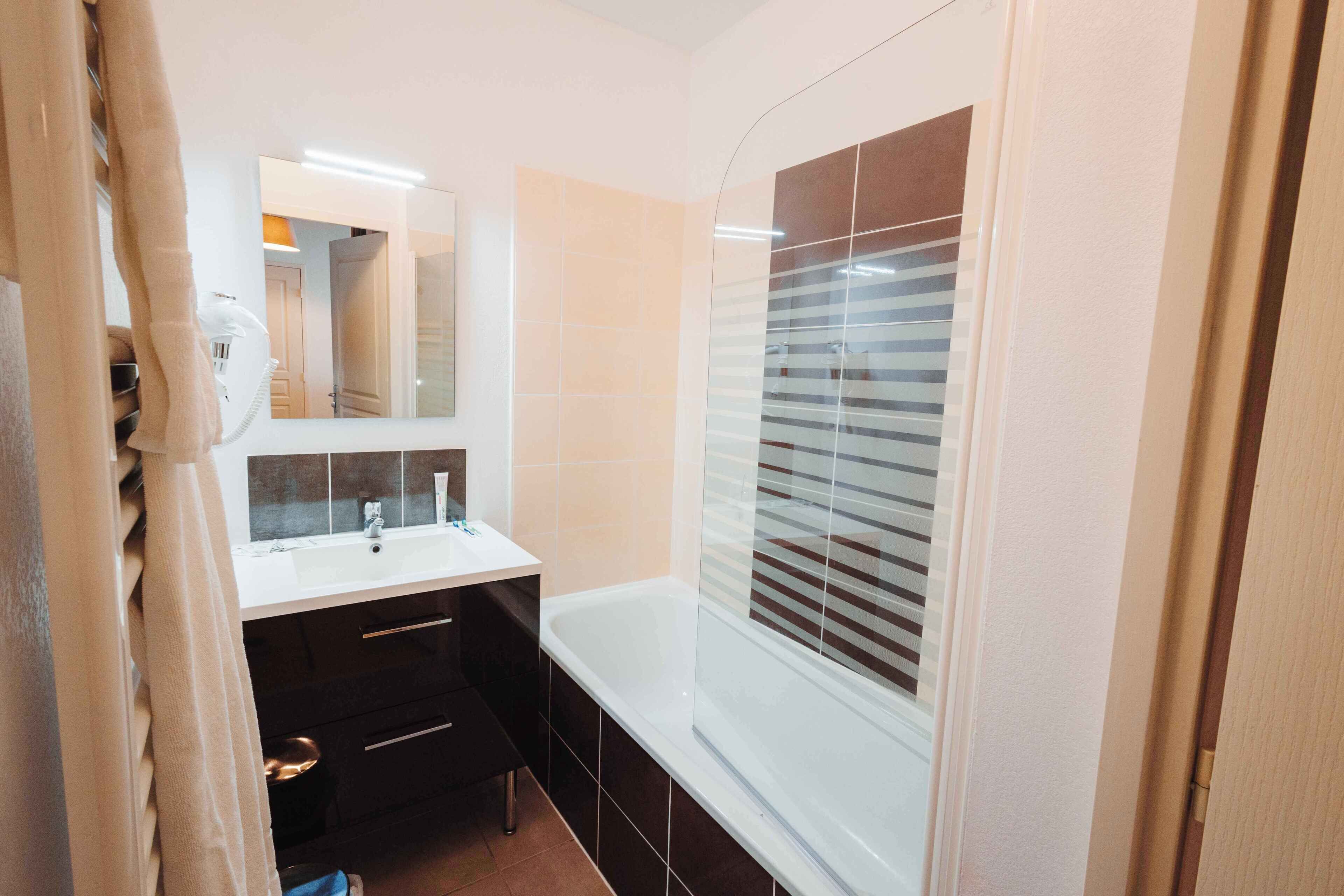 A modern bathroom with a white sink, dark cabinetry, and a large mirror.