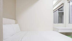 A single-bed room with a window, a bedside table, and a green chair. - Warm And Cozy 2Br At Pakubuwono Terrace Apartment (Jakarta)