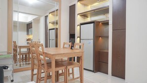 A modern kitchen with a wooden dining table and chairs, built-in cabinets, and a refrigerator. - Warm And Cozy 2Br At Pakubuwono Terrace Apartment (Jakarta)