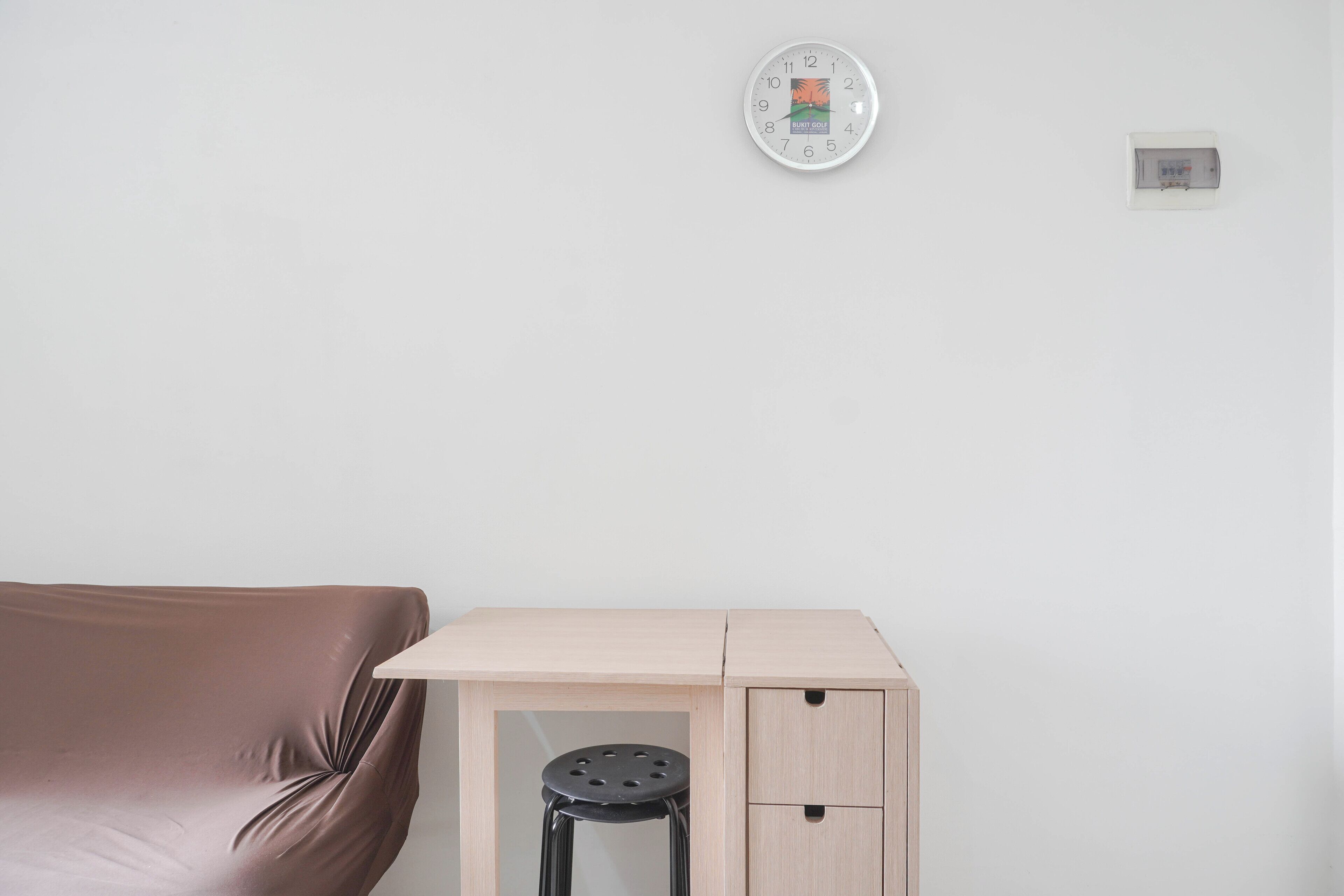 Een kamer met een bruine bank, een houten bureau met een kruk, en een wandklok.