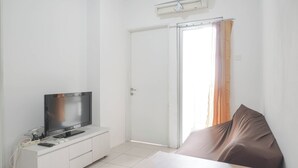Une pièce avec un téléviseur posé sur un meuble blanc, une porte avec un rideau et un lit avec un oreiller marron.