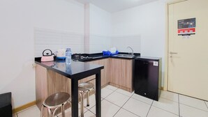 A compact kitchen with a black countertop, stainless steel stools, a sink, and a small refrigerator. - Comfort Living And Homey 2Br Apartment M-Town Residence (Gading Serpong)