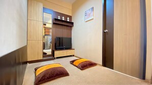 Une chambre de taille modeste, comprenant un lit, une télévision, une armoire et une petite étagère ornée d’objets décoratifs.