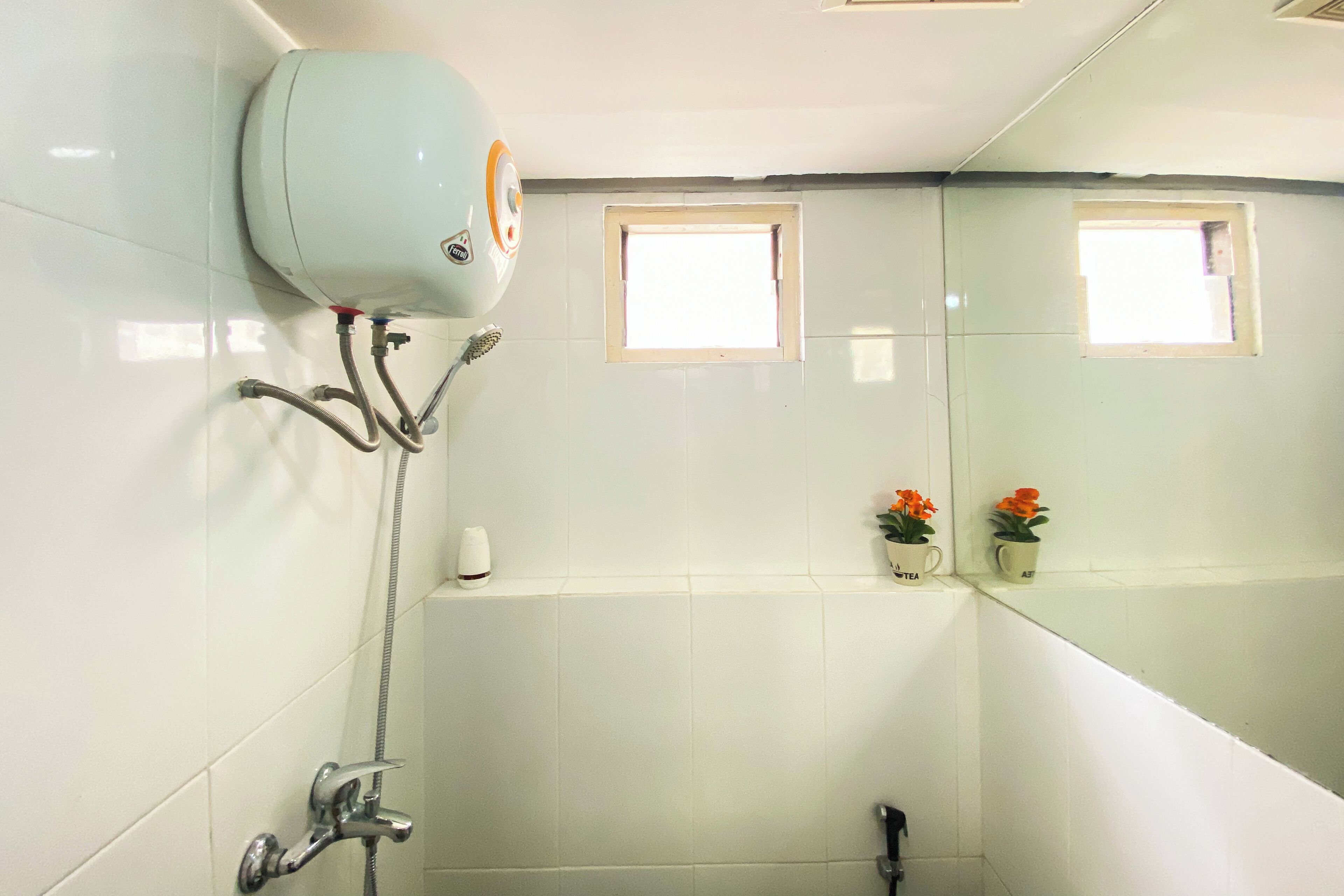 Une salle de bain avec des carreaux blancs, une douche, des toilettes et deux petites fenêtres.