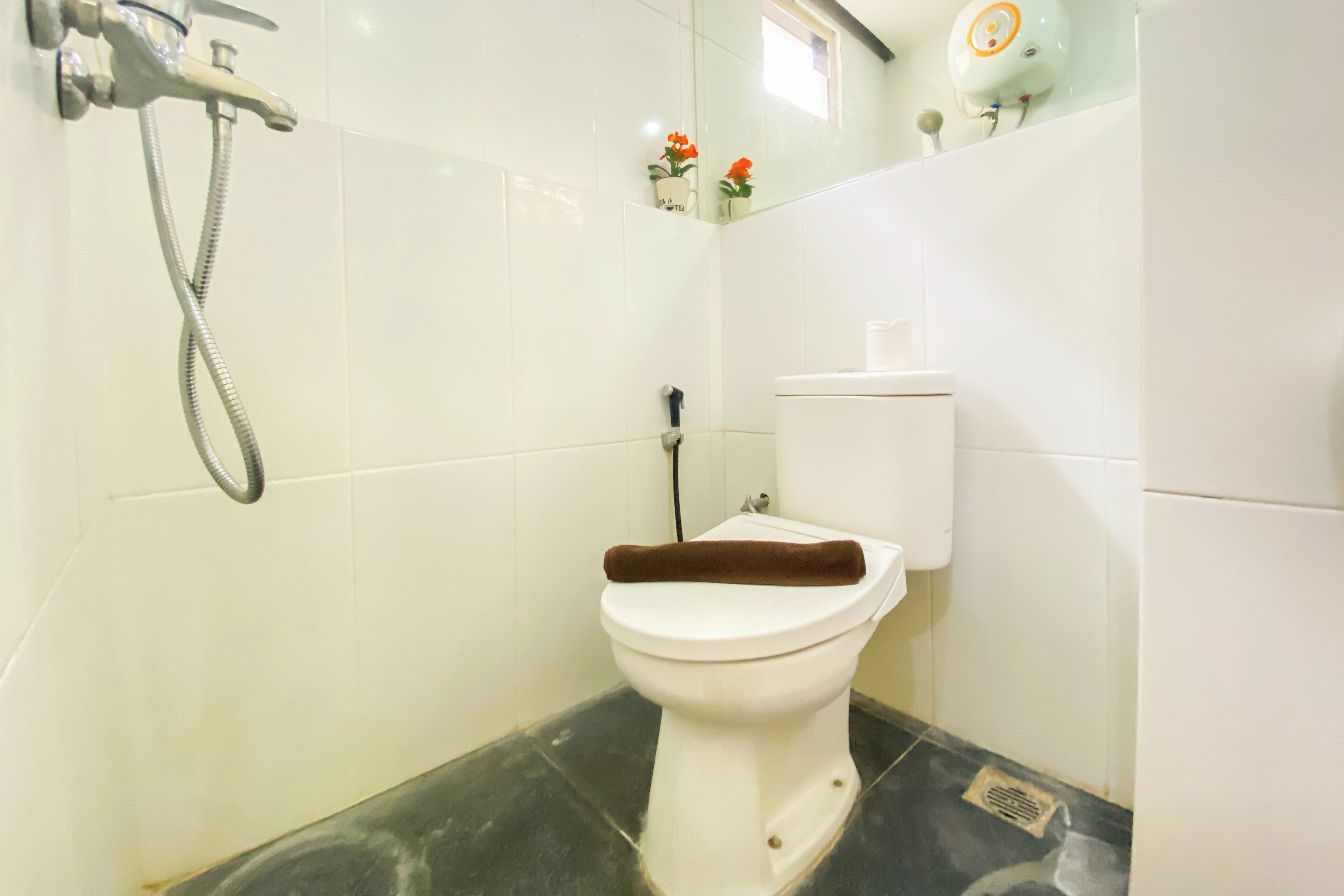 A bathroom with a toilet, a shower, and a small window with flowers.