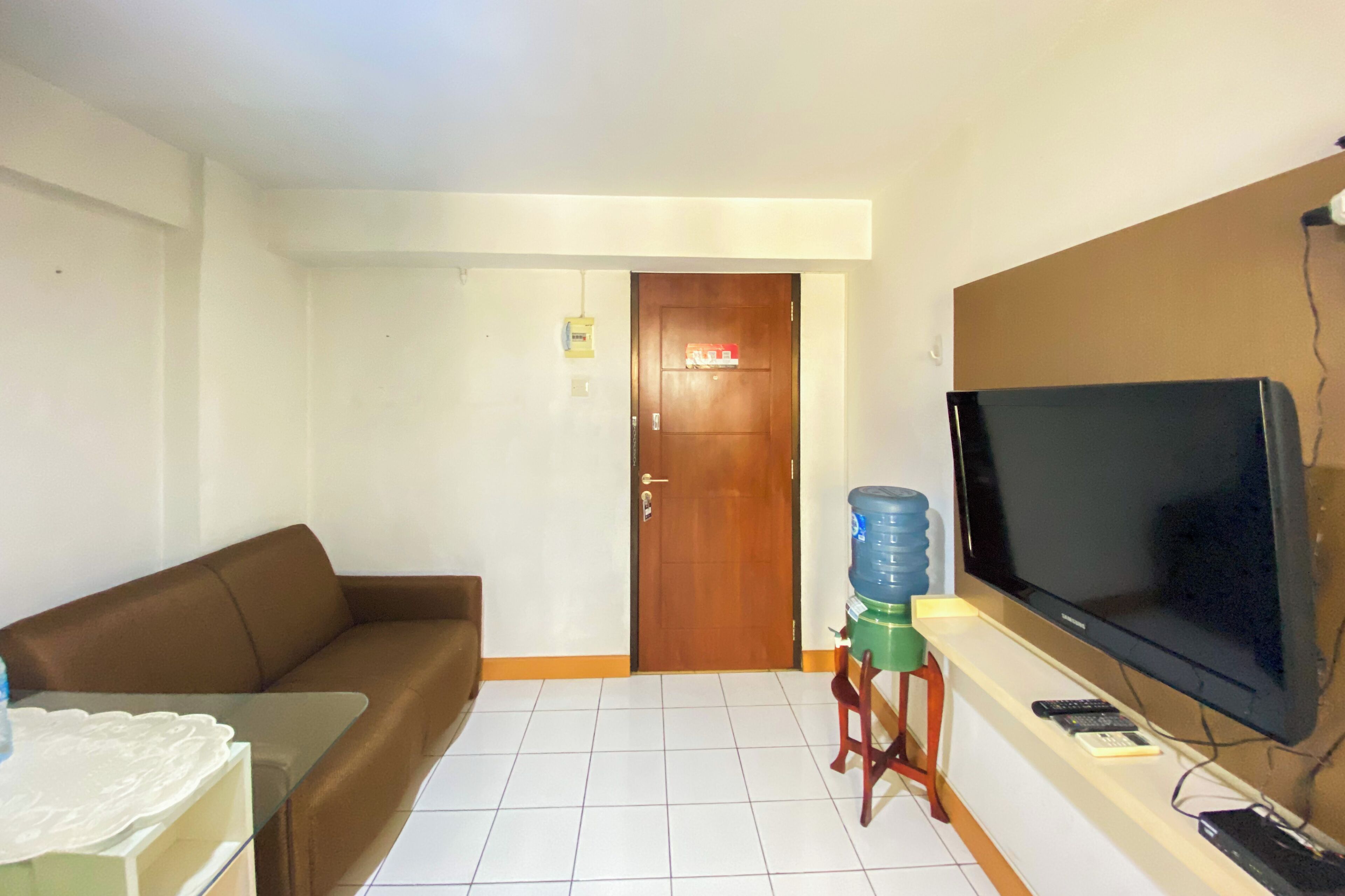 A living room with a brown sofa, a glass coffee table, a TV on a stand, and a water dispenser.