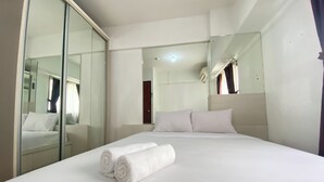 A hotel room with a large bed, a glass partition wall, and a mirror reflecting the room. - Homey 2Br With Modern Design Kebagusan City Apartment (Jakarta)