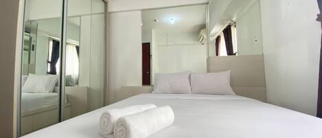 A hotel room with a large bed, a glass partition wall, and a mirror reflecting the room.