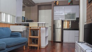 Un espacio habitable compacto con sofá, una mesita de madera, una kitchenette equipada con refrigerador y microondas, y un televisor.
