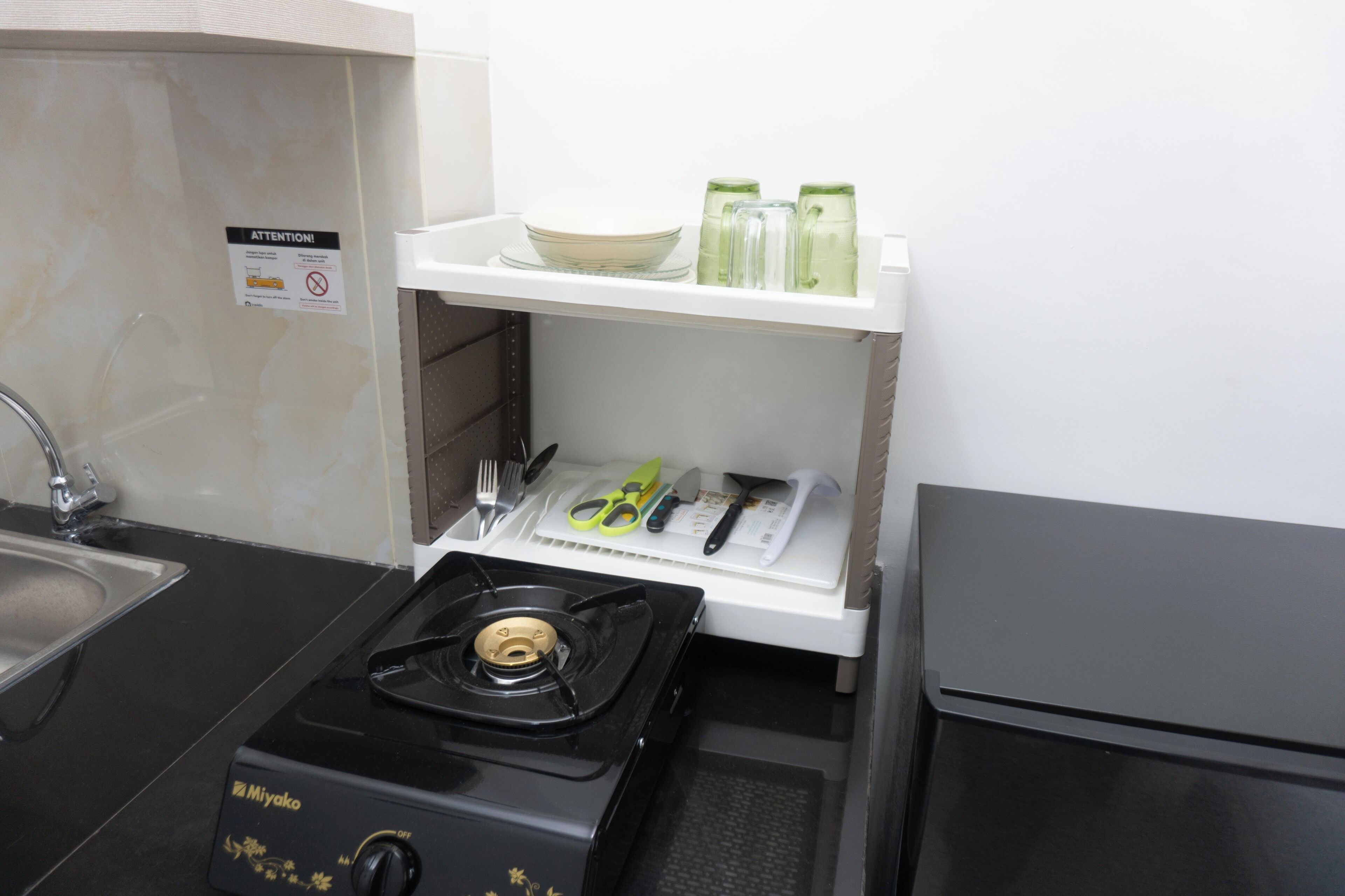 A kitchen with a gas stove, a sink, and a shelf with kitchen utensils.
