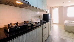 A modern kitchen with a gas stove, a microwave, and a sink. There is a window providing natural light and a view of the outside. - Minimalist Designed And Nice Studio At Bintaro Icon Apartment (South Tangerang)