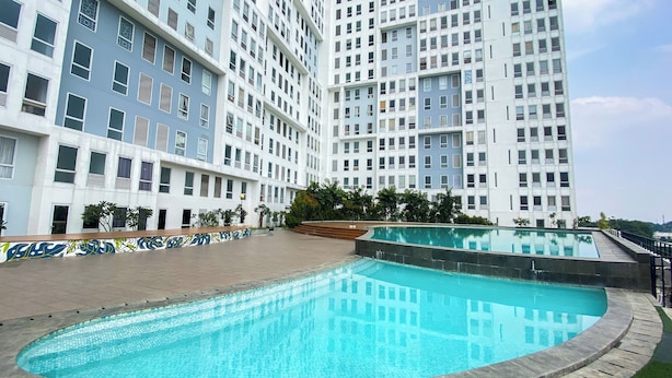 A modern building with a pool area, featuring a curved pool and a tiled walkway. - Studio Patraland Urbano Apartment (Bekasi)